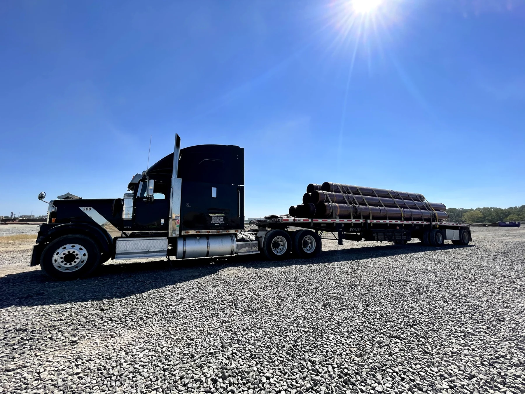 Dark EDOTEX tractor with pipe secured on its flatbed trailer