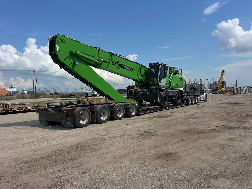Large green material handler secured on a specialized low trailer